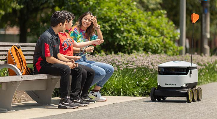 Students sitting on bench looking at food robot